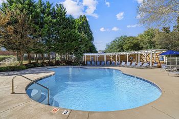 A large outdoor swimming pool surrounded by trees and lounge chairs.